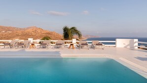 A swimming pool with lounge chairs and a table, overlooking a mountainous landscape and the sea. - Princess Estate in Mykonos (Mykonos)