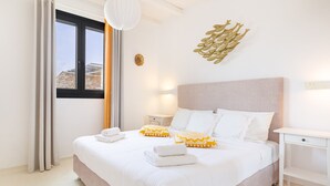 A hotel room with a bed, bedside tables, a window with curtains, and a wall-mounted light fixture. - Princess Estate in Mykonos (Mykonos)