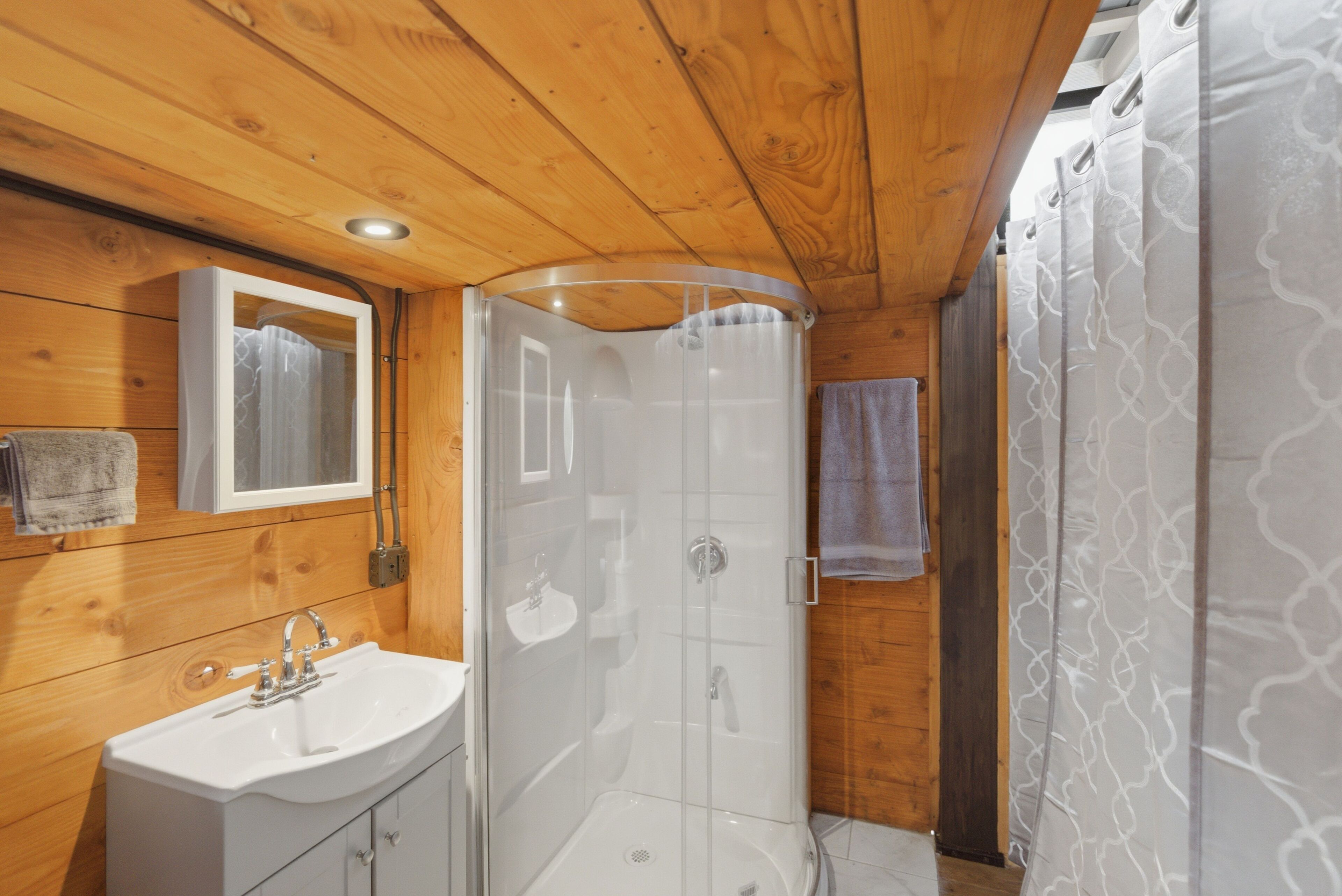 A wooden cabin bathroom with a sink, mirror, shower, and patterned shower curtain.