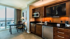 A hotel room with a large window, a dining table, a kitchen area with a microwave, a coffee maker, and a flat-screen TV mounted above the counter. - Stunning MGM Studio Strip View 16611 (Las Vegas)