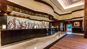 Un hall d’accueil d’hôtel moderne, doté d’un comptoir d’accueil incurvé, d’un grand mur orné d’un motif décoratif et d’un espace d’attente spacieux avec un tapis à motifs.