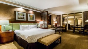 Une chambre d’hôtel avec un grand lit, un bureau, une chaise, un banc et une vue sur l’extérieur, visible à travers une porte vitrée.