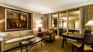 Une chambre d’hôtel avec un canapé, un fauteuil, une table à manger et un grand tableau au mur.