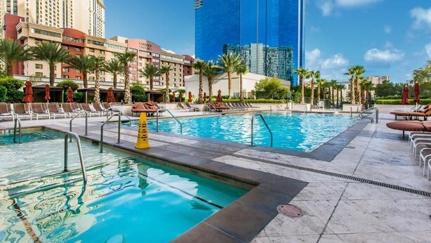 Ein Hotelpoolbereich mit mehreren Pools, Palmen und einem großen, blauen Gebäude im Hintergrund.