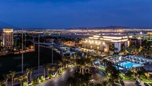 Un hotel con piscina, palmeras y vistas a un paisaje urbano nocturno.