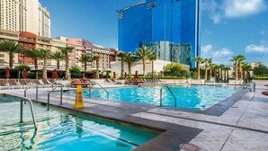 Un área de piscina de hotel con una piscina azul cristalina, palmeras y un edificio moderno al fondo.