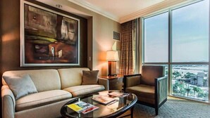 A hotel room with a sofa, armchair, coffee table, and a large window offering a city view. - Stunning MGM Studio Strip View 26611 (Las Vegas)