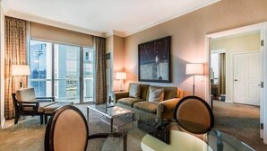 Hotellihuone, jossa on sohva, nojatuoleja, lasinen sohvapöytä, taulu seinällä ja näkymä suurista ikkunoista.