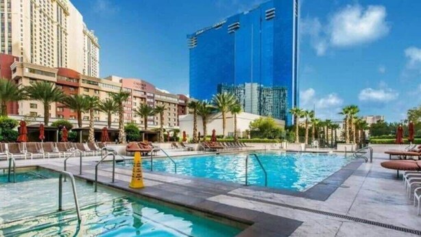 Area piscina di un hotel con diverse piscine, palme e un grande edificio blu sullo sfondo.
