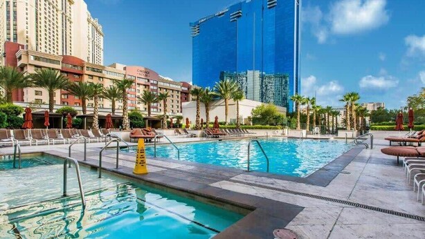 A hotel pool area with multiple pools, palm trees, and a modern building in the background. - New* Stunning MGM Studio Strip View 10609 (Las Vegas)