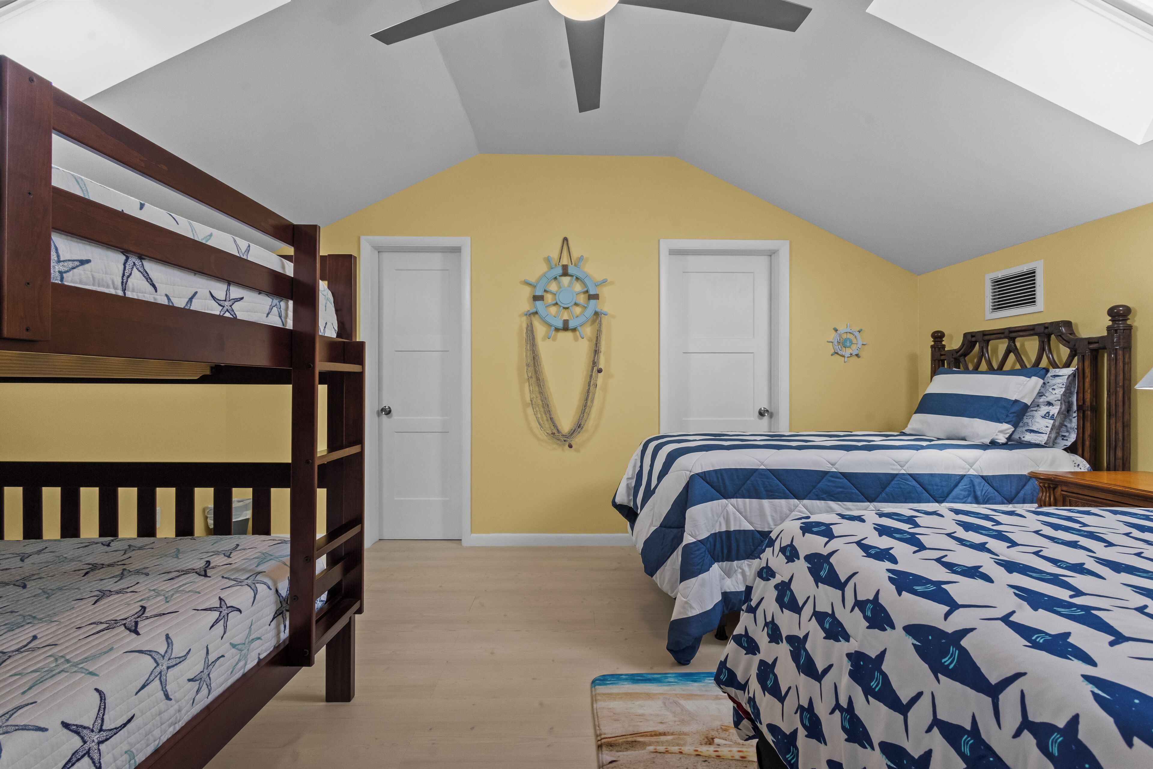 A bedroom with bunk beds, a bed with a striped bedspread, and nautical-themed wall decor.