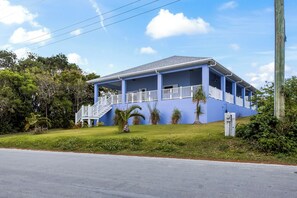 A two-story house with a blue exterior, a front porch with white railings, and a staircase leading to the entrance. - Family Friendly Pink Sand Beach House Sleeps 10 with Ocean Views (Spanish Wells)