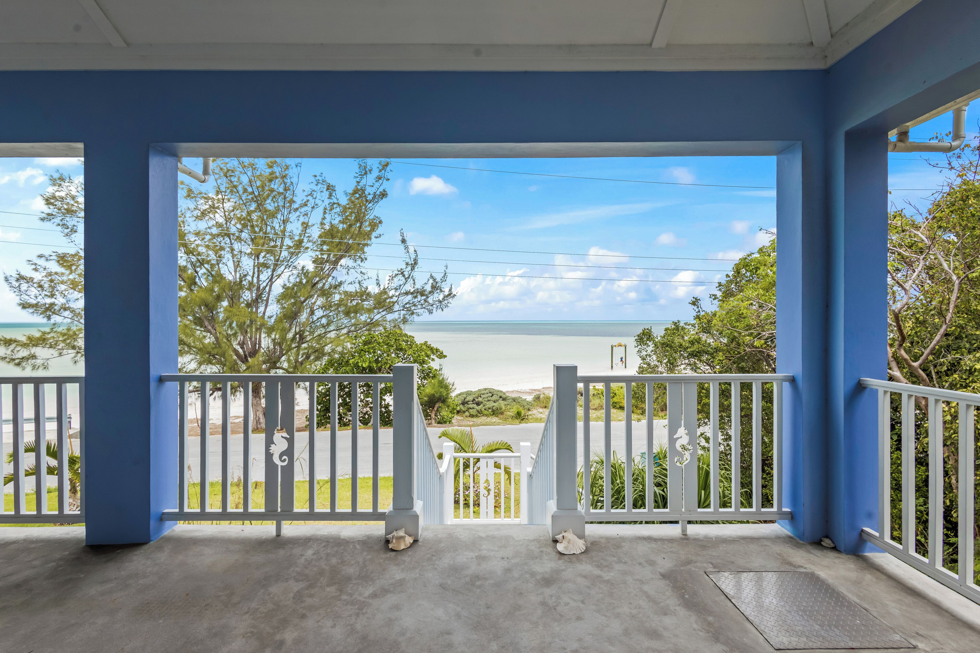 A covered porch with a view of the ocean and a parking area.