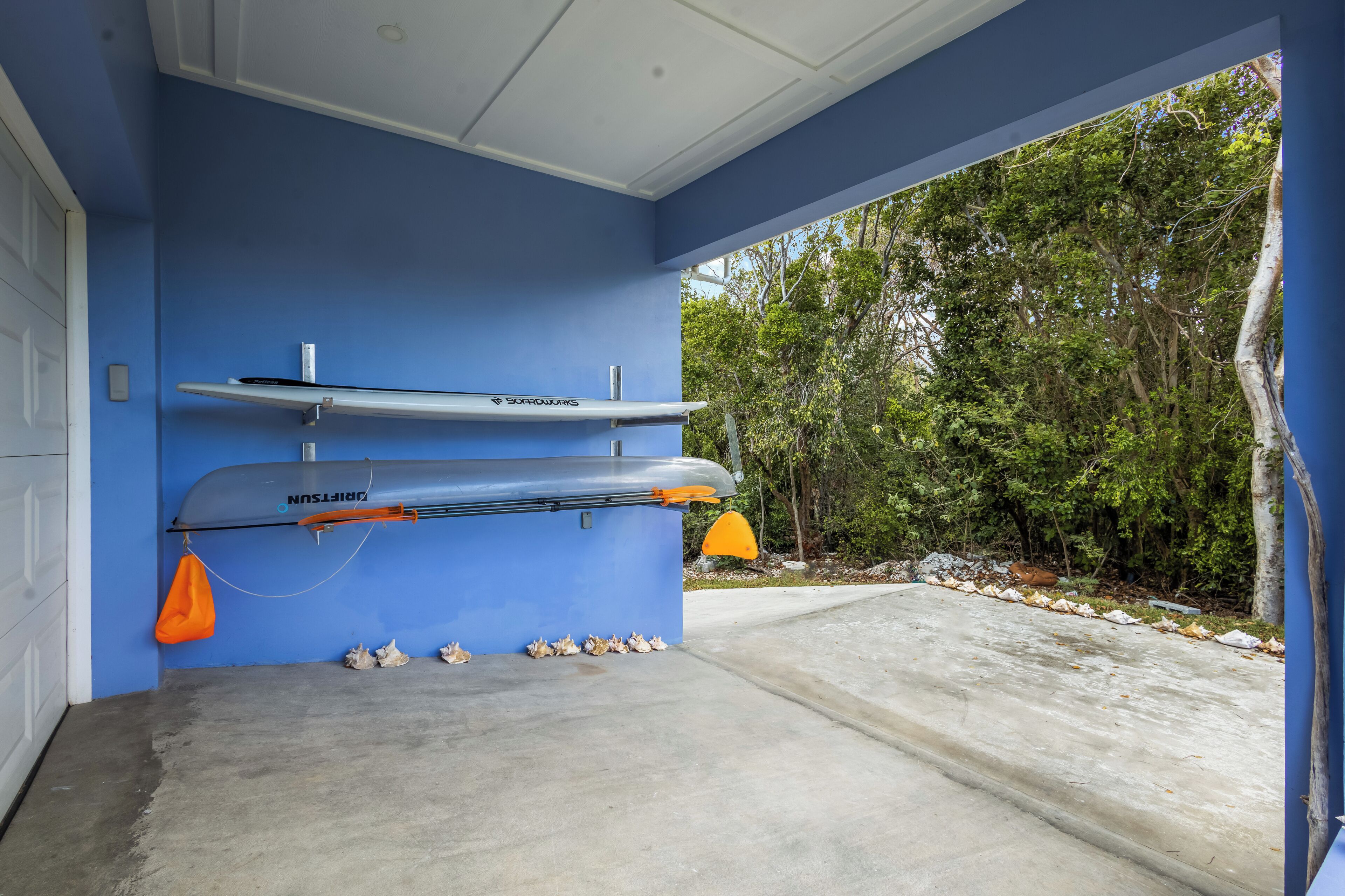 Un garage avec deux kayaks fixés au mur, un sol en béton et une vue sur une zone boisée.