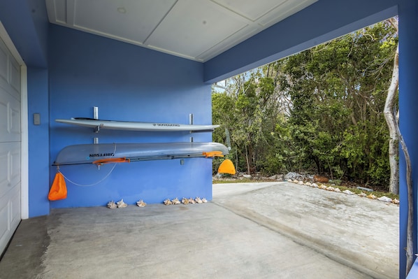 Un garaje con dos kayaks colgados en la pared, suelo de hormigón y vista a zona boscosa.