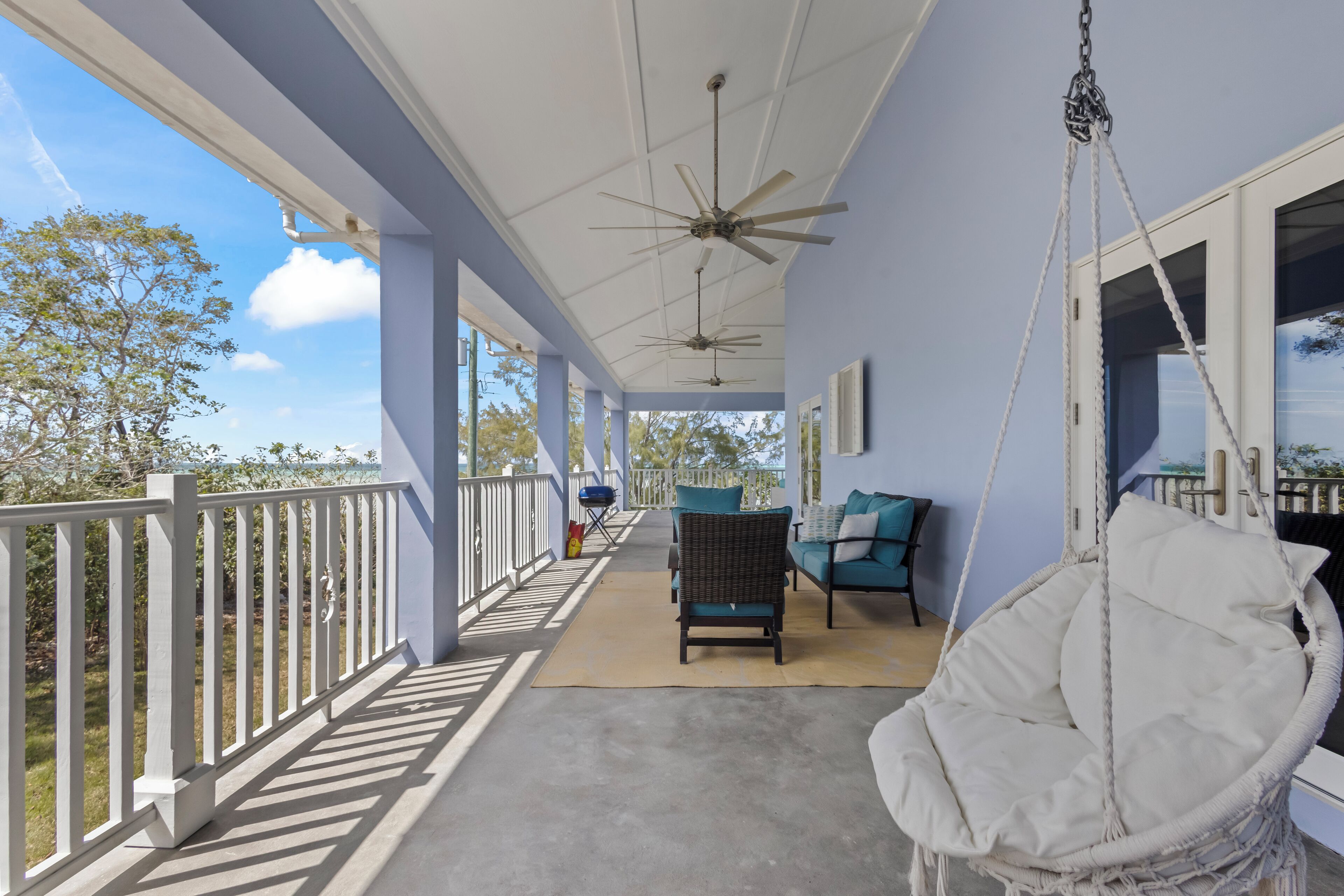 A covered porch with a swing chair, a seating area with cushions, and a ceiling fan.