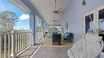 A covered porch with a swing chair, a seating area with cushions, and a ceiling fan.