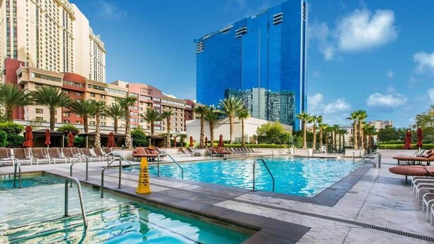 Ein Hotelpoolbereich mit mehreren Pools, Palmen und einem modernen Gebäude im Hintergrund.