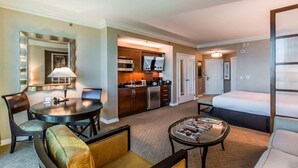 Habitación de hotel con una mesa de comedor, un sofá, una mesa baja, un televisor, una zona de cocina y una cama.