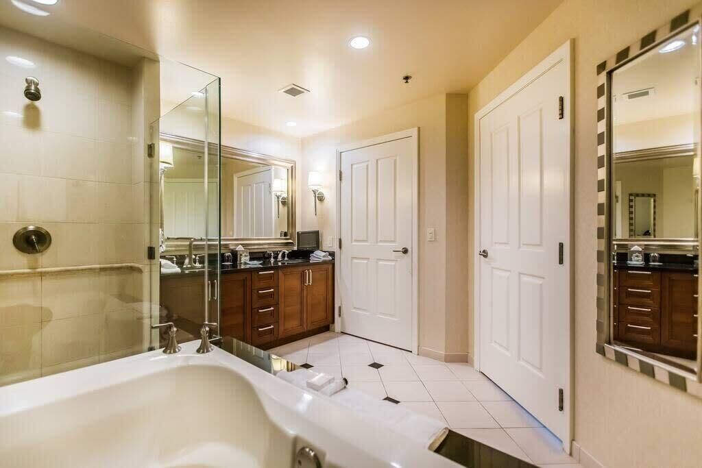 A modern bathroom with a large bathtub, a vanity with a mirror, and two white doors.