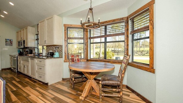 Una cocina con armarios de madera, una mesa redonda de madera y ventanas amplias.