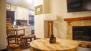 Una sala de estar con chimenea, una mesa redonda de madera, un sillón mecededor y un televisor montado en la pared.