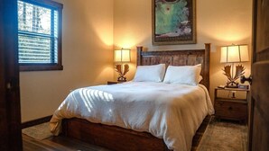 Una cama bien hecha con un cabecero, dos mesitas de noche con lámparas, una ventana con persianas y un cuadro colgado en la pared.