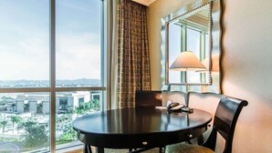 Una camera d'albergo con un'ampia finestra, un tavolo rotondo con una lampada e una sedia.