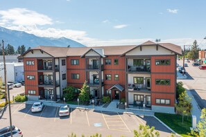 Ein mehrstöckiges Hotel mit Balkonen, einem Parkplatz und einer Bergkulisse.