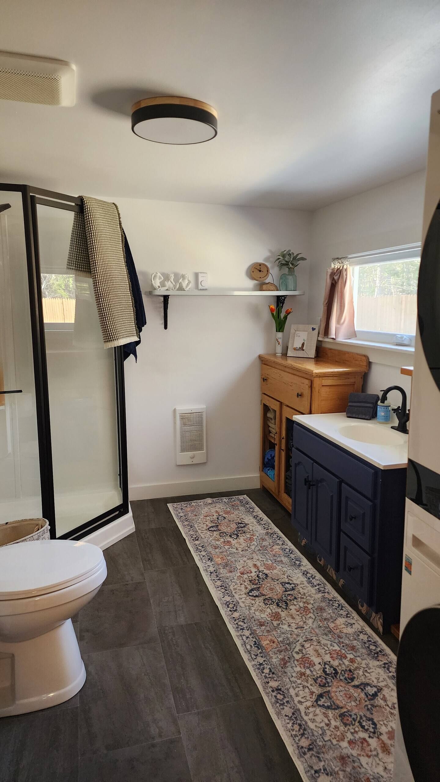 A compact bathroom with a shower, toilet, sink, and a decorative rug.