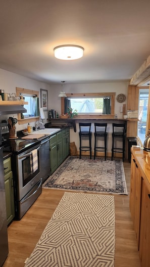 A kitchen with a stove, sink, and bar stools.