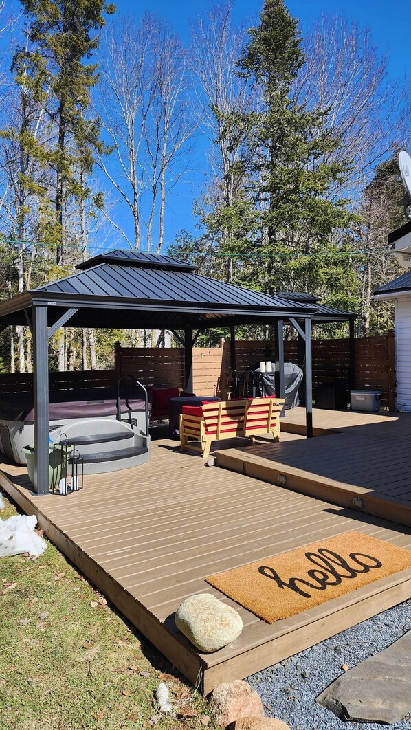 A covered outdoor seating area with a barbecue grill, a wooden deck, and a welcome mat.