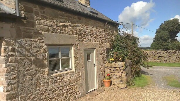 A stone house with a door, a window, and a small garden area with a potted plant. - Cosy Cottage Retreat. Log Burner. Courtyard & Starry Skies (Consett)