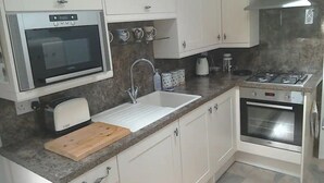 A kitchen with white cabinets, a microwave, a sink, a toaster, a cutting board, a stove, and a gas range. - Cosy Cottage Retreat. Log Burner. Courtyard & Starry Skies (Consett)