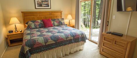 A bedroom with a bed, two bedside lamps, a television on a stand, and a sliding glass door leading to a balcony.