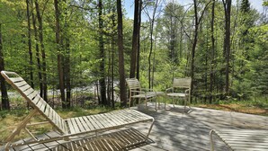 Eine Holzterrasse mit Liegestühlen und einem Tisch in einem bewaldeten Gebiet.