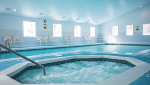 A large indoor swimming pool with a hot tub in the center, surrounded by white chairs and benches. - Spacious 2 bdrm, 2 Bath with Loft, 1500 Sq Ft. Many onsite amenities with Golf/Skiing near by! (Harbor Springs)
