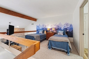 Une chambre avec deux lits, un banc en bois, une télévision et une fresque murale sur le thème de la montagne.