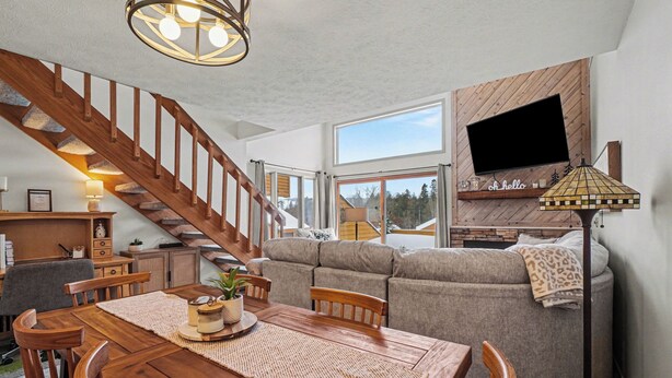 A spacious living area with a wooden staircase, a sofa, a dining table with chairs, and a TV mounted on the wall. - Spacious 2 bdrm, 2 Bath with Loft, 1500 Sq Ft. Many onsite amenities with Golf/Skiing near by! (Harbor Springs)