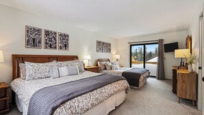 A hotel room with a large bed, two bedside tables, a desk, a chair, a TV, and a sliding glass door to the outside. - Spacious 2 bdrm, 2 Bath with Loft, 1500 Sq Ft. Many onsite amenities with Golf/Skiing near by! (Harbor Springs)