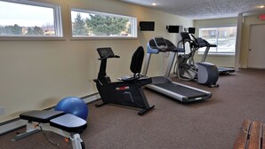 Een sportschool met loopbanden, een elliptische machine, een hometrainer en een blauwe fitnessbal.