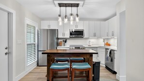 A modern kitchen with white cabinets, stainless steel appliances, a wooden island with stools, and pendant lighting. - Enjoyable 1-bedroom 1-bath condo in charming Marco Island. (Marco Island)
