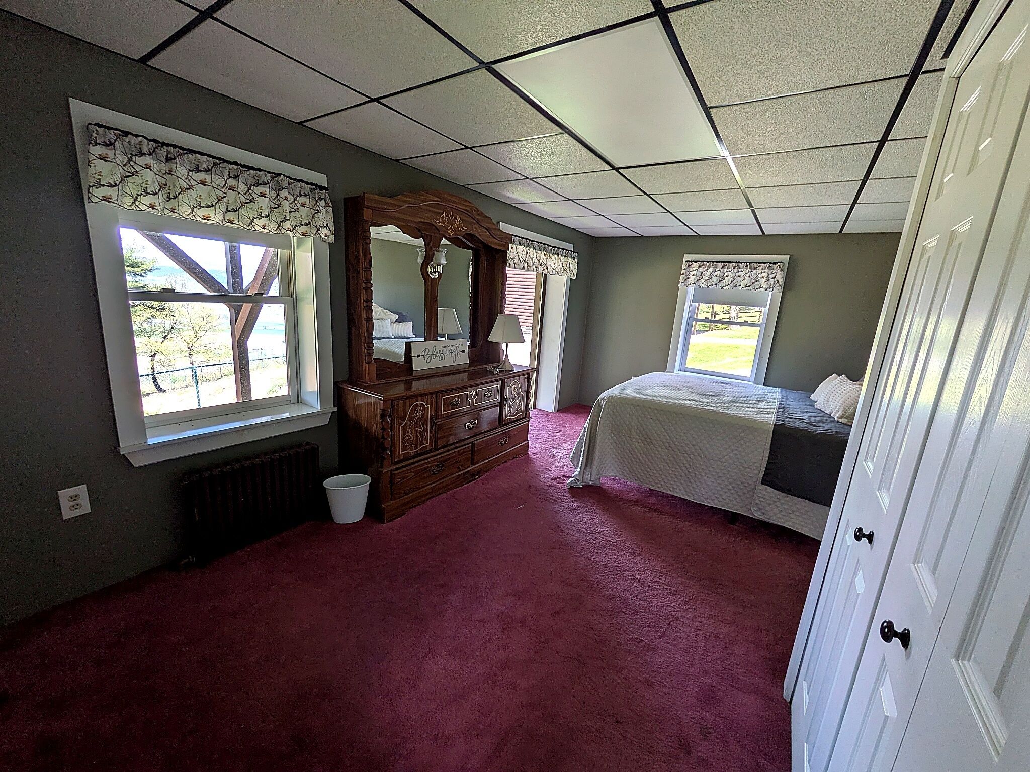 Een slaapkamer met een groot bed, een dressoir, een spiegel en twee ramen.