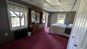 Een slaapkamer met een groot bed, een dressoir, een spiegel en twee ramen.