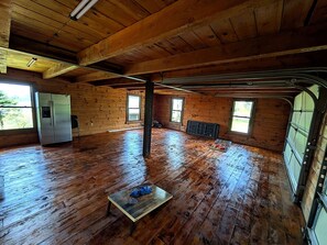 A spacious room with wooden floors, a refrigerator, a bench, and large windows. -  Enjoy a beautiful log cabin overlooking Belleville, PA with stunning views (Belleville)