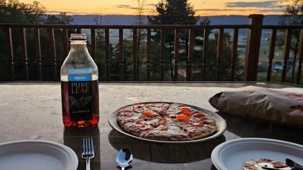 Une table avec une bouteille de vin, une pizza et des assiettes, le tout installé sur une terrasse offrant une vue magnifique.