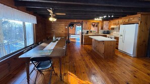 L’intérieur d’une cabane en bois comprend une table à manger, des chaises, un coin cuisine et un ventilateur de plafond.