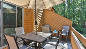 Une terrasse en bois avec une table et des chaises, un grand parasol et une vue sur une forêt.