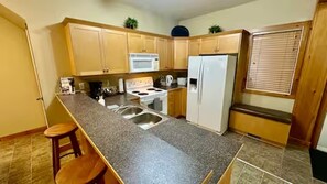 A kitchen with a granite countertop, stainless steel sink, white appliances, wooden cabinets, and a window with blinds. - Ski & Golf Getaway Suite - private hot tub - 2 bed (Kimberley)