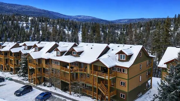 A multi-story lodge with a snow-covered roof, wooden balconies, and a mountainous backdrop. - Ski & Golf Getaway Suite - private hot tub - 2 bed (Kimberley)